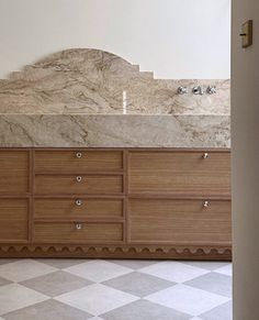 an empty bathroom with marble counter tops and drawers on the wall, in front of a checkered tile floor