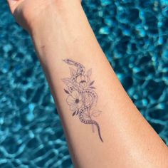 a woman's arm with flowers and a snake tattoo on her left wrist next to a swimming pool