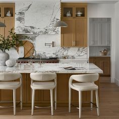 a kitchen with marble counter tops and white chairs in front of an island that has two vases on it