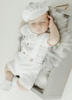 a baby laying on top of a box wearing a white hat and dress with feathers