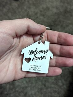 a hand holding a house shaped keychain with the words welcome home on it