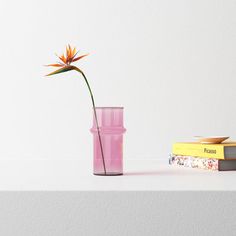 a pink vase with a flower in it next to some books on a white table