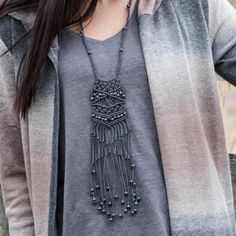 a woman wearing a gray shirt with a black tasseled necklace on her neck