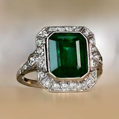 A striking platinum ring that centers a natural emerald weighing approximately 4.32 carats with vivid green color. Surrounding the center gemstone is a row of old-cut diamonds which continues along the shoulders. This ring features a detailed under-gallery.
The measurements of this ring, including the diamond halo, are 15.05mm x 13.20mm.
This ring can be resized to any finger size at no extra cost.
Ready to Make It Yours? Contact us to reserve this ring and to get more info! Zambia Emerald Ring, Art Deco Green Ring, Gia Certified, Art Deco Green Ring Gia Certified, Green Octagon Diamond Ring, Luxury Green Octagon Rings, Elegant Green Octagon Diamond Ring, Gia Certified Green Emerald Art Deco Ring, Exquisite Green Emerald Ring With Halo Setting, Octagon Green Emerald Ring With Center Stone