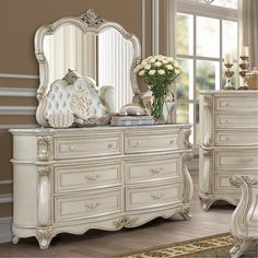 an ornate white dresser and mirror in a room with flowers on the table, and a vase filled with roses