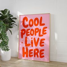 a pink poster with the words cool people live here on it next to a potted plant