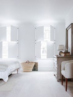 a white bedroom with two windows and a bed in the corner next to a dresser