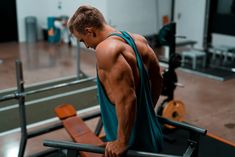 a man with no shirt on standing in front of a gym bench and looking down at his back