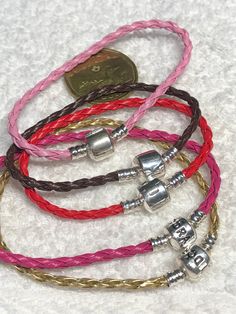 four different colored bracelets with silver clasps on white fabric, one has a coin in the background