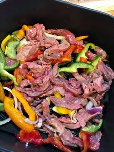 a pan filled with meat and vegetables on top of a wooden table next to utensils