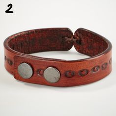 a close up of a leather bracelet on a white surface with two metal circles and holes in the middle