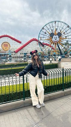 a woman standing next to a fence near a roller coaster