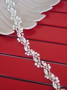 a white plate sitting on top of a red table next to a silver and crystal necklace