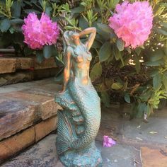 a statue of a mermaid sitting on top of a stone floor next to pink flowers