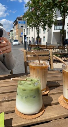 two drinks are sitting on a table with a woman taking a photo in the background