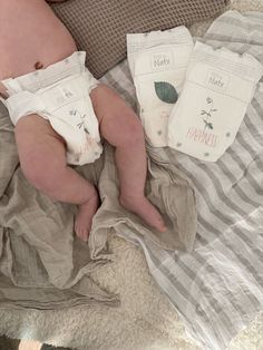 a baby laying on top of a bed next to three diapers