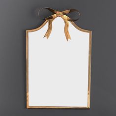 a gold framed mirror with a bow on the top and bottom edge, hanging on a gray wall