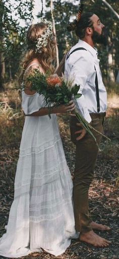 a man and woman standing in the woods with flowers on their foreheads, looking at each other