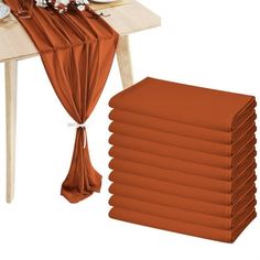 a stack of orange napkins sitting on top of a wooden table next to a white plate