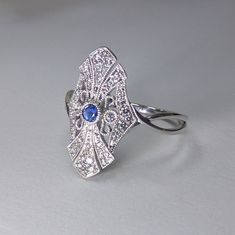 Art Deco Diamond & Blue Sapphire Fashion Ring, Filigree Design 14k White Gold DIAMOND DETAILS: Shape: Round Cut Diamonds Number of Stones: 44 Carats: 0.20 ct. Clarity: VS-SI - Eye Clean Color: H-I GEM STONES: Shape: Round Cut Blue Sapphire Number of stones: 1 Approx. 0.05 ct. Clarity: Eye Clean Color: Medium Blue SETTING: Material: 14k White Gold (Available Also in 14K Yellow Gold or 14K Pink Gold - No Extra Charge) Ring size 7 (custom made in other sizes) Comes packaged In Pop up gift box S Art Deco Blue Diamond Ring With Accents, Blue Art Deco Diamond Ring With Accents, Fine Jewelry With Accent Stones For Collectors, Art Deco White Gold Jewelry With 17 Jewels, Blue Art Deco Diamond Ring With Diamond Cut, Blue Diamond Ring, Art Deco Style, Gift, Sapphire And Diamond Accented Platinum Jewelry, Art Deco Blue Cubic Zirconia Rings, Art Deco Blue Diamond Ring Gift