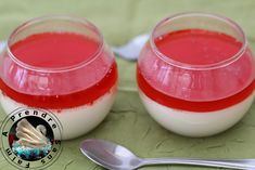 two glasses filled with red liquid sitting on top of a table next to spoons