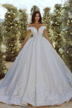 a woman in a wedding dress standing next to an archway with flowers and greenery