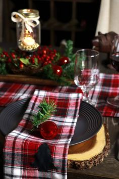 a christmas table setting with red and white plaid napkins, black plates, silverware and greenery