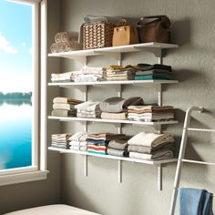 a white shelf filled with lots of folded clothes next to a window in a room