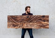 a man holding up a large wooden sign that looks like wavy lines on it's surface