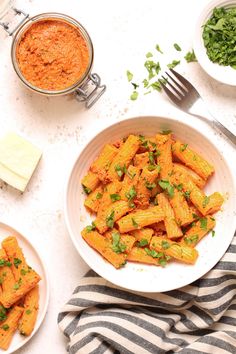 two bowls filled with pasta and sauce on top of a striped towel next to other dishes