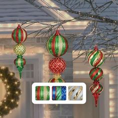 christmas ornaments hanging from a tree in front of a house decorated with lights and garlands