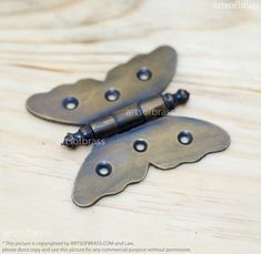 two antique style metal hinges with holes on them sitting on a wooden surface