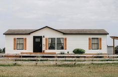 a small white house sitting on top of a grass covered field next to a wooden fence