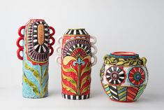 three colorful vases sitting next to each other on a white surface with no one around them