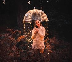 a woman standing in the woods holding an umbrella with fairy lights strung all over it