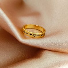 a gold ring with hearts on it sitting on a pink silk fabric, close up