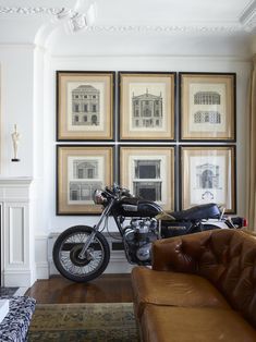 a motorcycle is parked next to a couch in front of some framed pictures on the wall