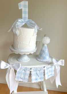 a white cake sitting on top of a table next to a baby's first birthday hat