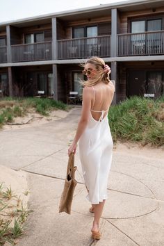 a woman in a white dress is walking down the sidewalk with her hand on her hip