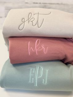 three sheets with embroidered monogrammed names on them, one in pink and the other in blue