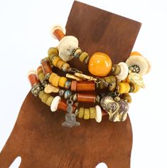 Beaded Stretch Bracelets. Indulge in the unique charm of these handmade Stackable Bracelets, designed to add a touch of boho chic to your style. Crafted with an array of materials including Horn, Czech glass, orange resin, bone, brass, and Thailand rustic glass.  These bracelets are versatile enough for solo wear or for stacking with others. The earthy color palette of light orange, rustic yellow, brass and off white will complement various outfits. With a comfortable fit for small wrists ranging from 6" to 6.50", these bracelets are strung with professional stretch cord.  Delivered in a gift box or bag, they make for a perfect present or a stylish treat for yourself. Available per bracelet or mix and match. Complete set is available - see photos for pricing. 1.    Brass Buddha charm, Czec Bohemian Multi-strand Bracelets With Large Beads, Bohemian Charm Bracelet Bangle With Colorful Beads, Bohemian Orange Beaded Bangle Bracelets, Bohemian Orange Beaded Bangle Bracelet, Orange Bohemian Beaded Bangle Bracelet, Bohemian Orange Bangle Jewelry, Orange Bohemian Bangle Jewelry, Bohemian Brown Stretch Bracelet With Colorful Beads, Handmade Spiritual Multi-strand Wrap Bracelet