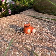 an orange cat keychain sitting on top of a stone slab with flowers in the background