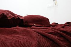 an unmade bed with red sheets and blankets on it's sides, in front of a white wall