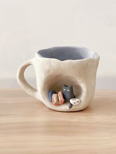 a ceramic cup with two cats in it sitting on a table next to a small cat figurine