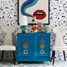 a blue cabinet with two white chairs and a painting on the wall above it in a living room