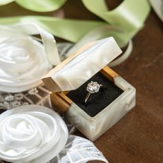 an engagement ring sits in a box on a table with ribbons and flowers around it