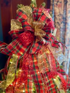 a christmas tree decorated with red, green and gold ribbons is shown in front of a window