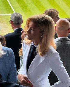 a woman in a white suit and tie standing next to other people at a baseball game