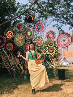 a woman standing in front of an array of colorful kites hanging from a tree