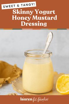 a glass jar filled with honey mustard dressing next to a sliced orange and a spoon